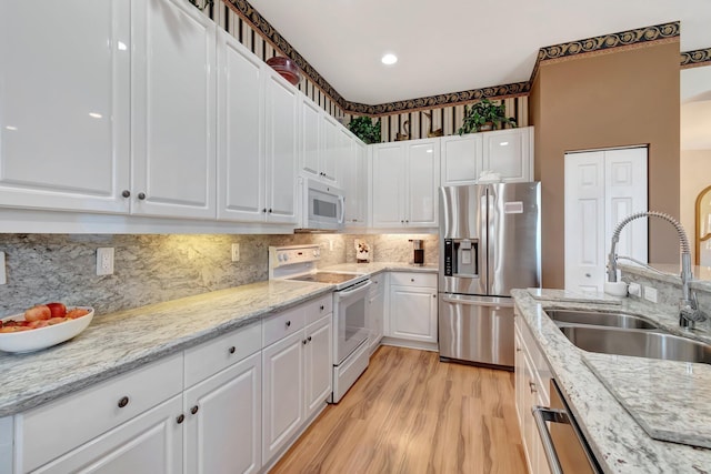 kitchen featuring stainless steel appliances, a sink, white cabinets, light wood-style floors, and decorative backsplash
