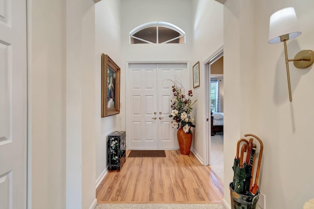 entryway featuring light wood-style flooring, a high ceiling, and baseboards