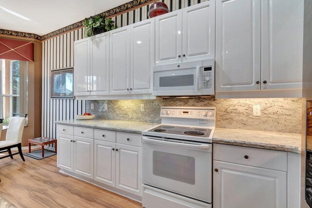 kitchen with white appliances, decorative backsplash, white cabinetry, light wood finished floors, and light stone countertops