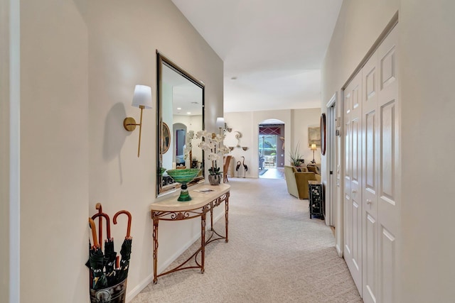 hall with arched walkways, light colored carpet, and baseboards