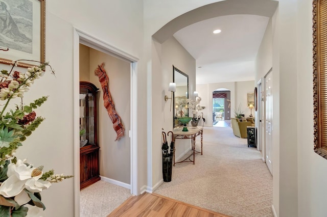 corridor featuring baseboards, arched walkways, carpet flooring, and wood finished floors