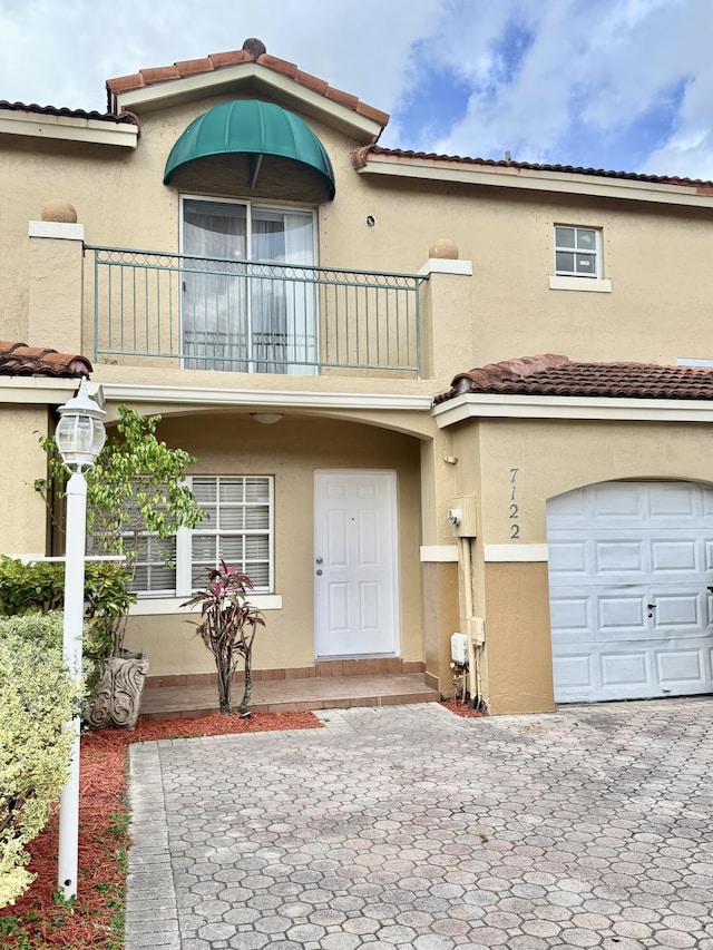 view of front of house with a tiled roof, a balcony, an attached garage, and stucco siding