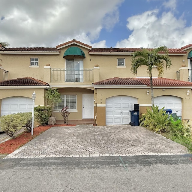 view of front of house with a balcony, an attached garage, a tile roof, and stucco siding