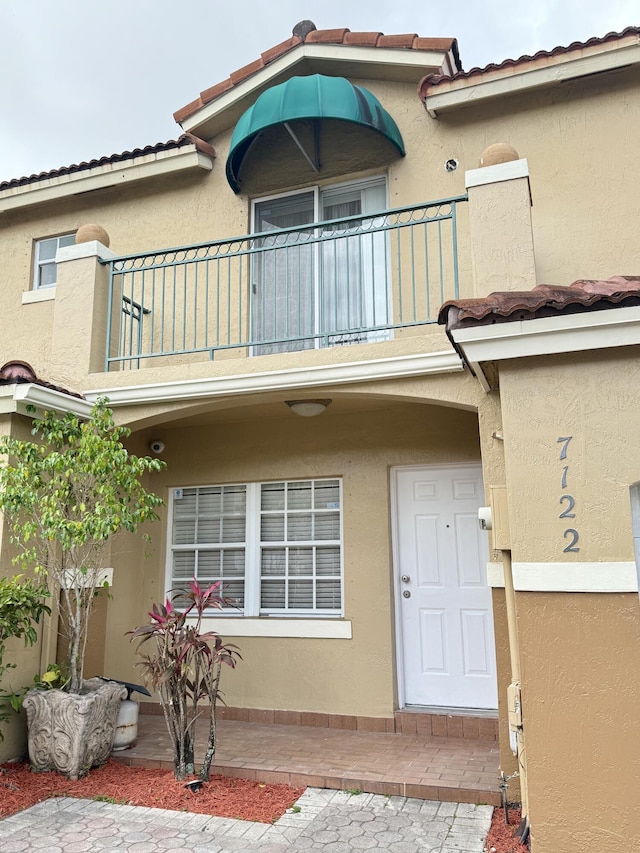 entrance to property featuring a tile roof, a balcony, and stucco siding