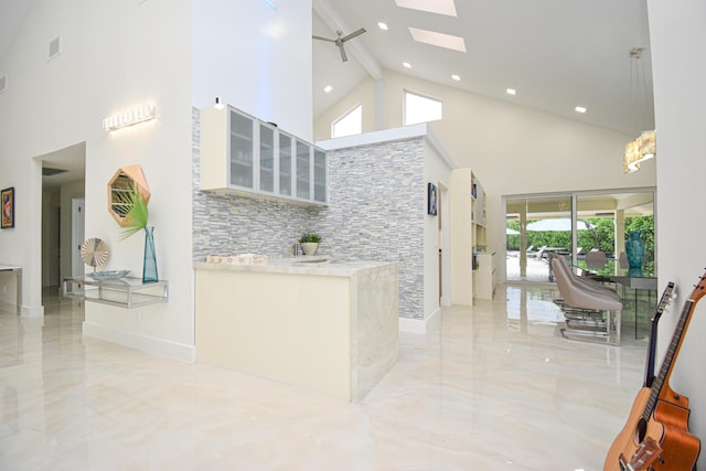 kitchen with a high ceiling, a skylight, glass insert cabinets, and marble finish floor