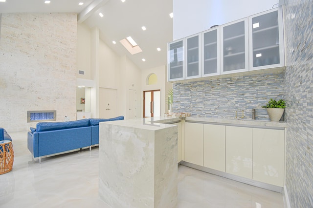 kitchen featuring glass insert cabinets, beam ceiling, a skylight, white cabinets, and high vaulted ceiling