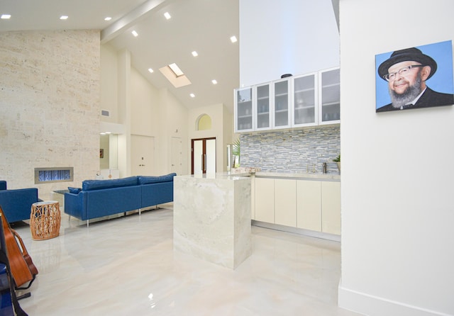 interior space featuring a skylight, glass insert cabinets, white cabinetry, backsplash, and a large fireplace