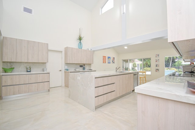 kitchen with modern cabinets, an island with sink, light brown cabinetry, a sink, and dishwasher