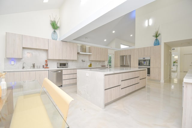 kitchen with modern cabinets, light brown cabinetry, a sink, appliances with stainless steel finishes, and wall chimney range hood