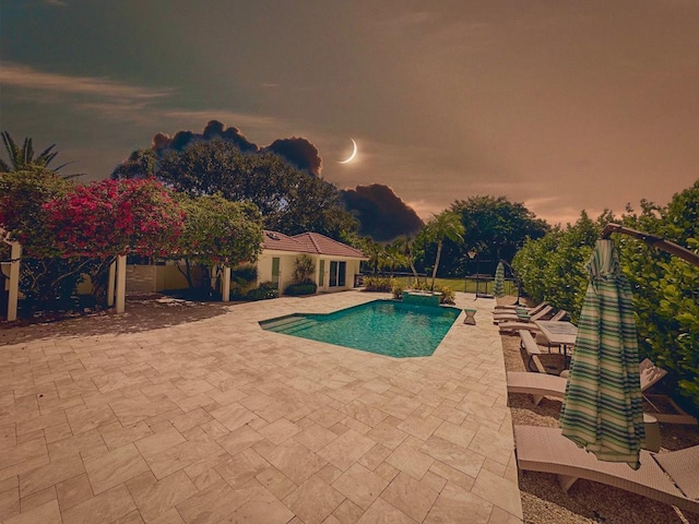 pool at dusk featuring a patio and a pool with connected hot tub