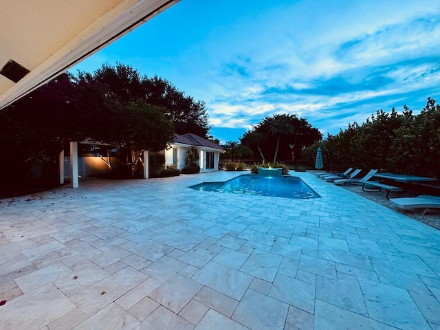 pool at dusk with a patio area, an outdoor pool, and an outdoor structure