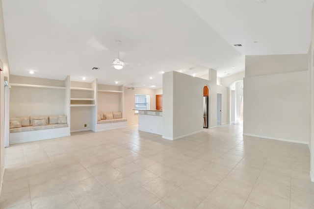 unfurnished living room with arched walkways, ceiling fan, lofted ceiling, visible vents, and baseboards