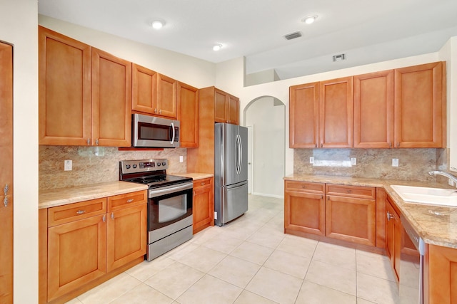 kitchen with arched walkways, tasteful backsplash, visible vents, appliances with stainless steel finishes, and a sink