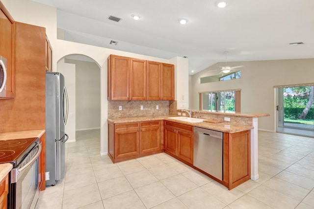 kitchen with arched walkways, a peninsula, a sink, appliances with stainless steel finishes, and tasteful backsplash