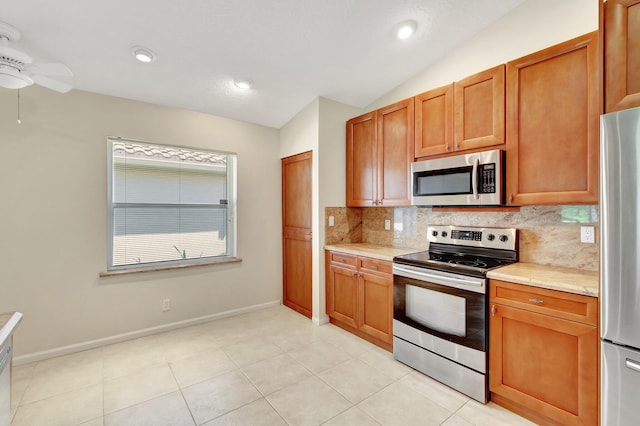 kitchen with baseboards, vaulted ceiling, appliances with stainless steel finishes, decorative backsplash, and brown cabinetry