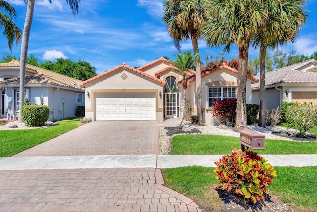 mediterranean / spanish-style house with stucco siding, a tiled roof, an attached garage, decorative driveway, and a front yard