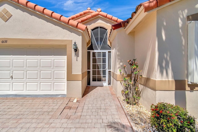 entrance to property with a garage, a tile roof, and stucco siding