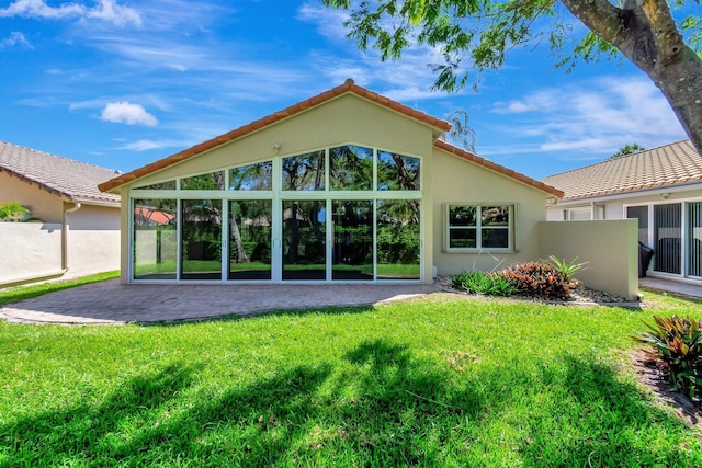 rear view of house with a tiled roof, a lawn, a patio area, and stucco siding