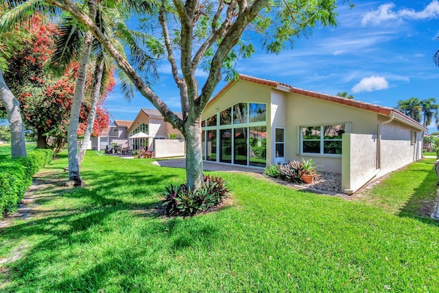 back of property with a yard, a tile roof, and stucco siding