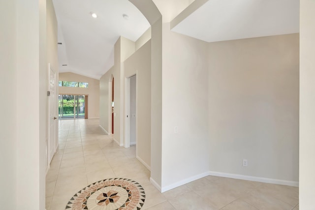 hall featuring light tile patterned flooring, vaulted ceiling, and baseboards