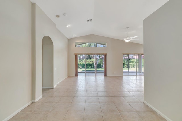 empty room featuring arched walkways, light tile patterned floors, visible vents, high vaulted ceiling, and baseboards