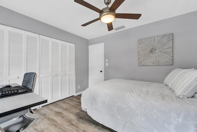 bedroom with a closet, visible vents, wood finished floors, and a ceiling fan
