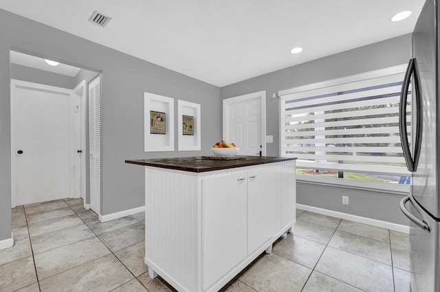 kitchen with white cabinets, baseboards, visible vents, and freestanding refrigerator