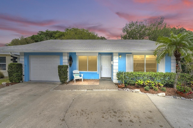 ranch-style house featuring stucco siding, driveway, roof with shingles, and an attached garage