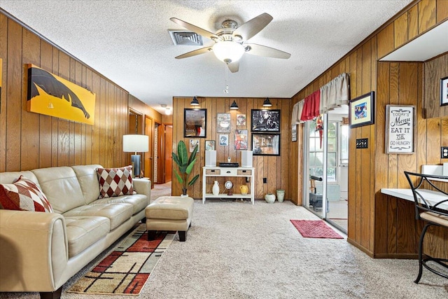 carpeted living area with visible vents, wood walls, a textured ceiling, and a ceiling fan