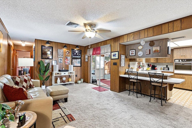 carpeted living area with a textured ceiling, visible vents, wood walls, and ceiling fan