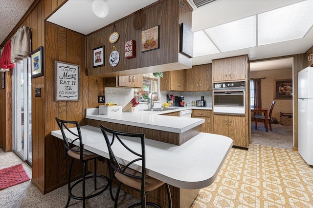 kitchen with white appliances, wooden walls, a peninsula, a sink, and light countertops