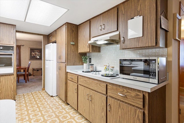 kitchen with under cabinet range hood, tasteful backsplash, white appliances, a skylight, and light countertops