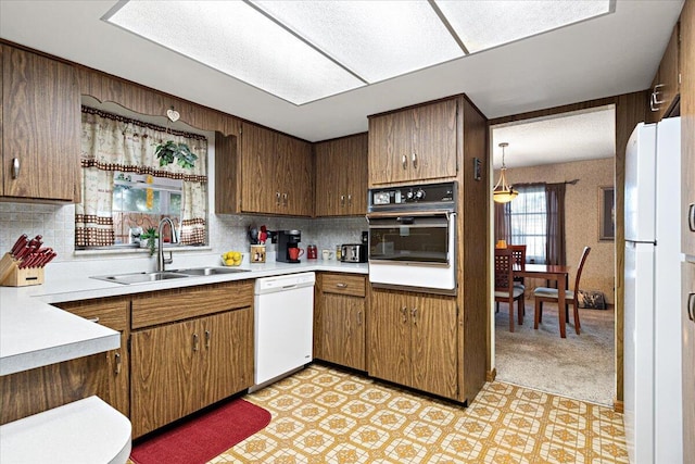 kitchen featuring light floors, light countertops, decorative backsplash, white appliances, and a sink