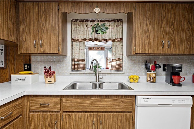 kitchen with white dishwasher, a sink, light countertops, brown cabinets, and backsplash