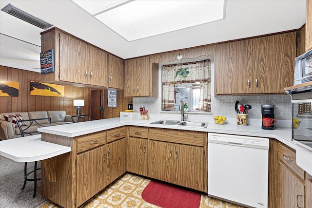 kitchen with a sink, dishwasher, a peninsula, and light countertops