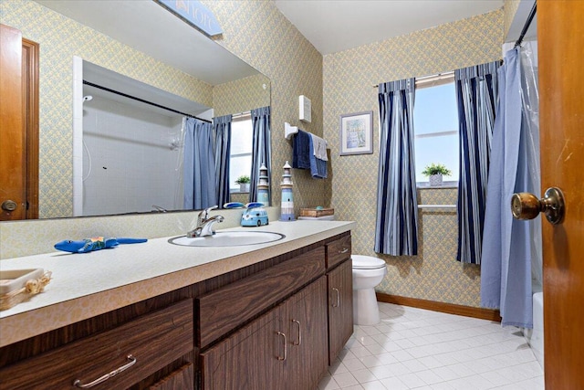 bathroom featuring baseboards, a healthy amount of sunlight, vanity, and wallpapered walls