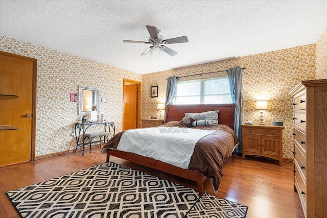 bedroom featuring wallpapered walls, light wood-style flooring, and a textured ceiling