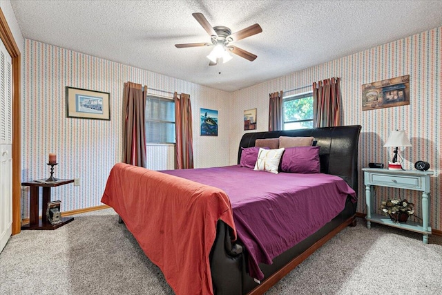 carpeted bedroom with a textured ceiling, wallpapered walls, baseboards, and a ceiling fan