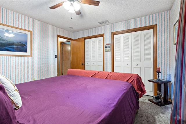 bedroom with wallpapered walls, two closets, and a textured ceiling