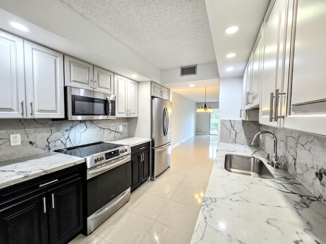 kitchen featuring stainless steel appliances, dark cabinetry, a sink, and light stone countertops