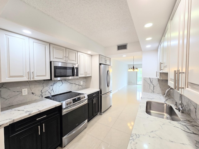 kitchen featuring stainless steel appliances, visible vents, white cabinetry, a sink, and dark cabinetry