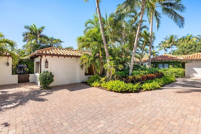 mediterranean / spanish-style home featuring stucco siding, a tile roof, decorative driveway, and a garage