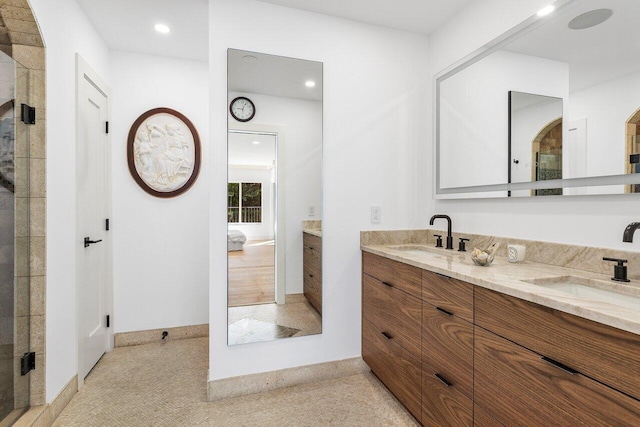 ensuite bathroom with double vanity, connected bathroom, a shower with door, and a sink