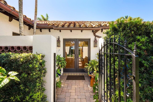 property entrance featuring stucco siding, french doors, a tile roof, and a gate