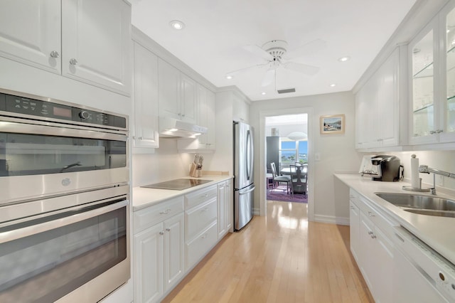 kitchen with under cabinet range hood, a sink, white cabinets, light countertops, and appliances with stainless steel finishes