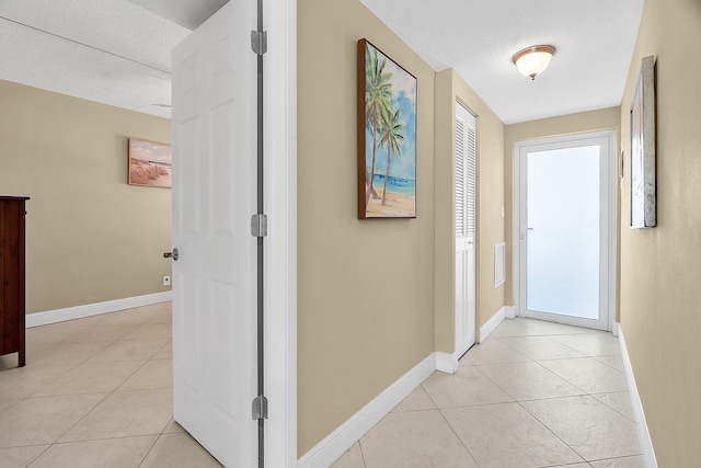 hall featuring visible vents, baseboards, a textured ceiling, and light tile patterned flooring