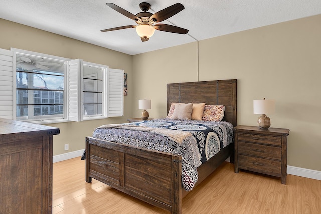 bedroom featuring baseboards, light wood-style floors, a ceiling fan, and a textured ceiling