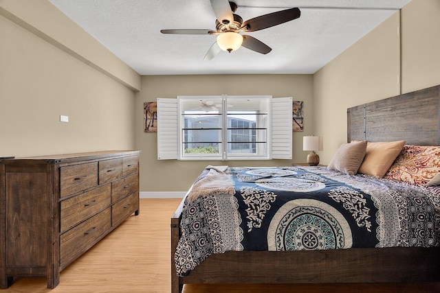 bedroom featuring ceiling fan, light wood-style flooring, baseboards, and a textured ceiling