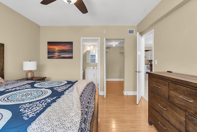 bedroom featuring visible vents, baseboards, light wood-type flooring, ensuite bathroom, and a ceiling fan