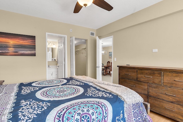 bedroom featuring ensuite bath, visible vents, light wood finished floors, and ceiling fan